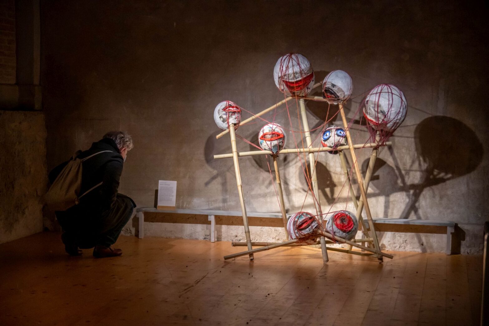 Installation von Bambuszweige an denen runde Ballone mit Augen und Münder. Neben dran eine Person liesst einen Text.