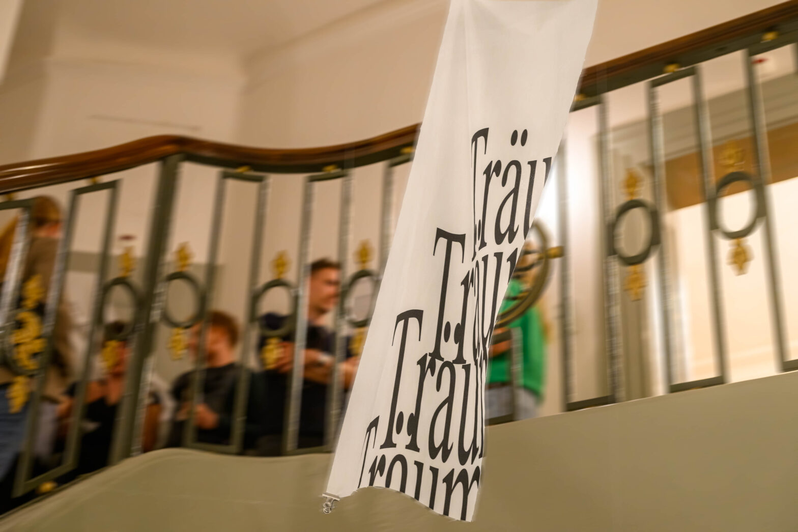Treppenhaus mit Menschen auf der Treppe in dessen Mitte ein Stück bedruckter weisser Stoff hängt, der in Bewegung zu sein scheint.