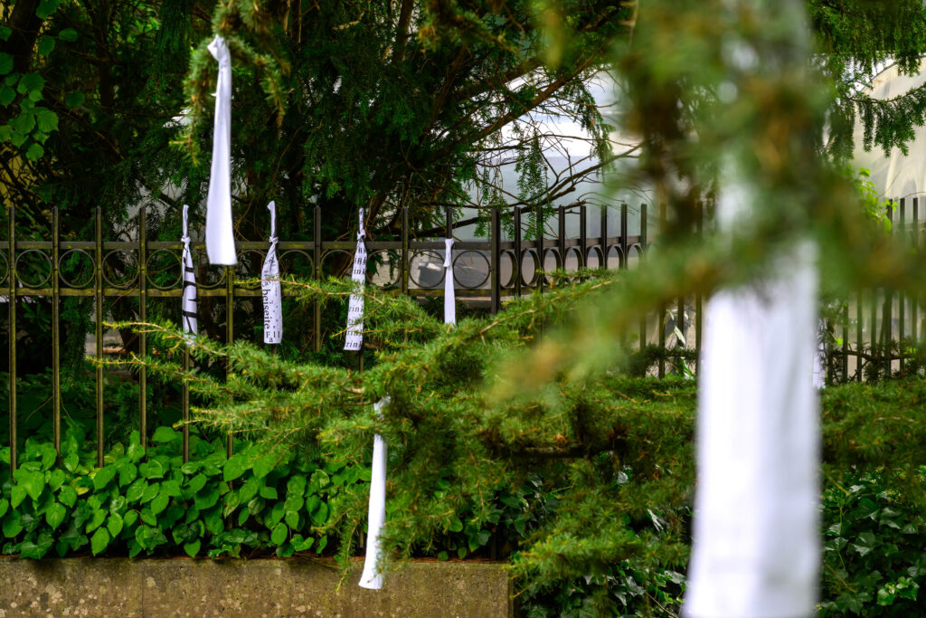 Weisse Stoffbänder mit gedrucktem schwarzen Text hängt geknotet an Ästen im Garten.