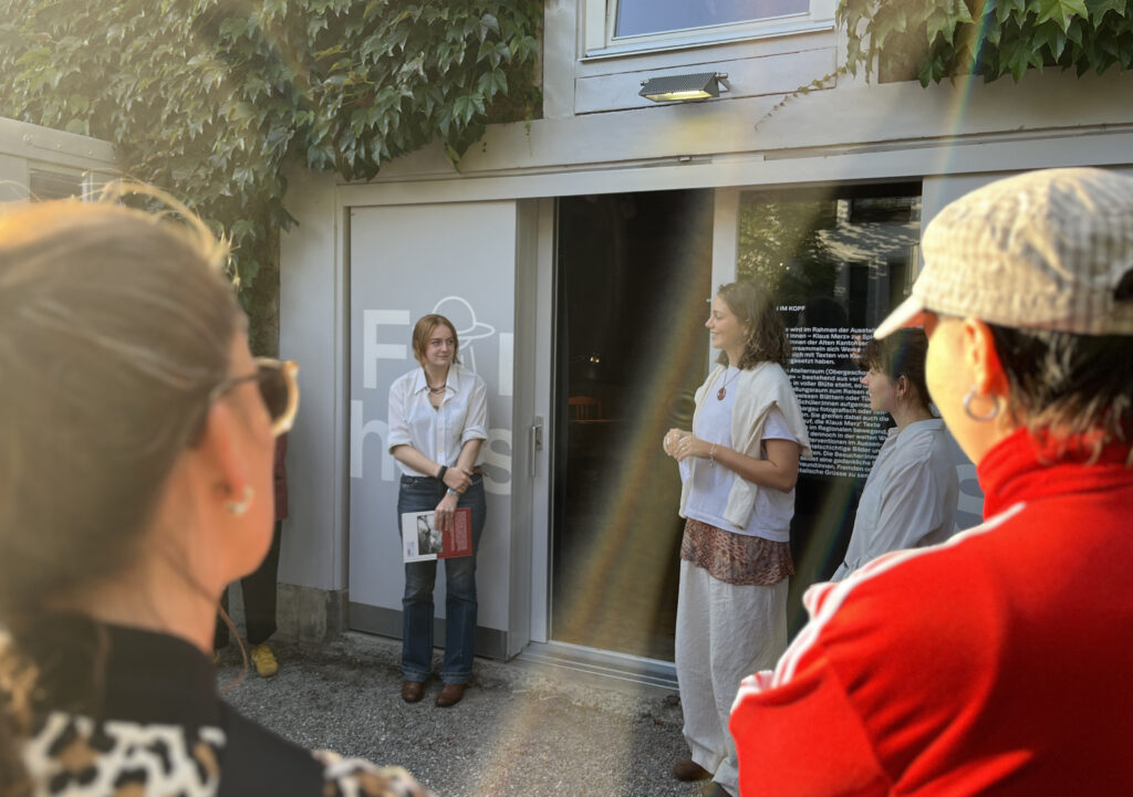 Zwei Schülerinnen stehen vor einer Eingangstüre und sprechen vor einem Publikum.