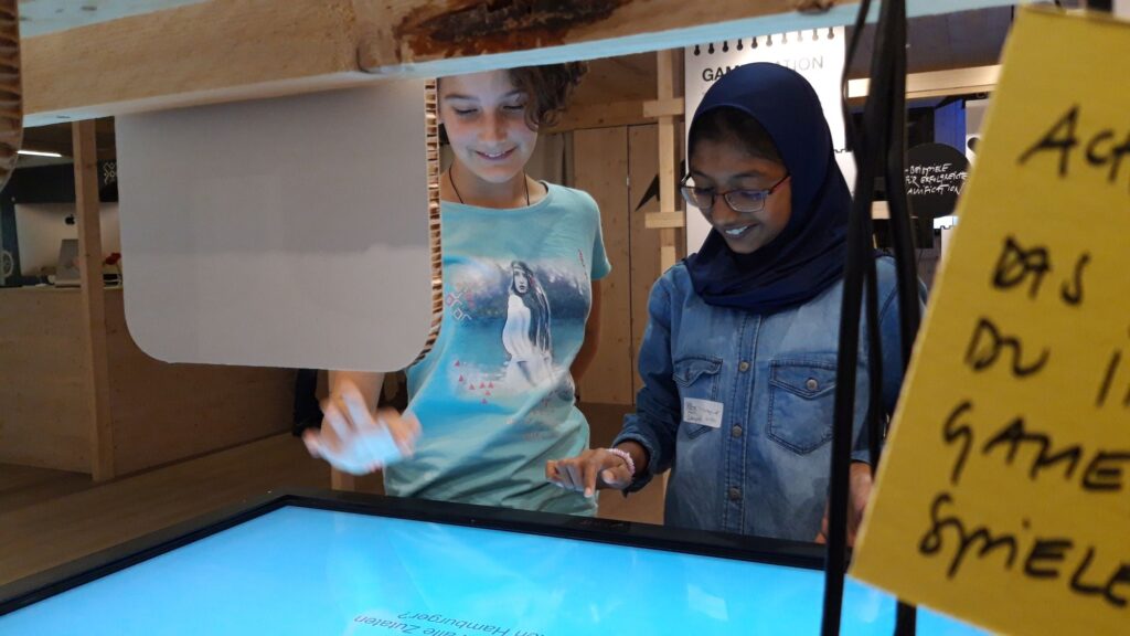 Zwei Schülerinnen tippen lächelnd auf einen Bildschirm.