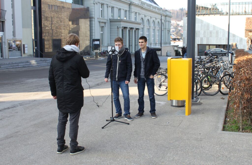 Drei junge Menschen moderieren mit technischer Ausrüstung im Freien.