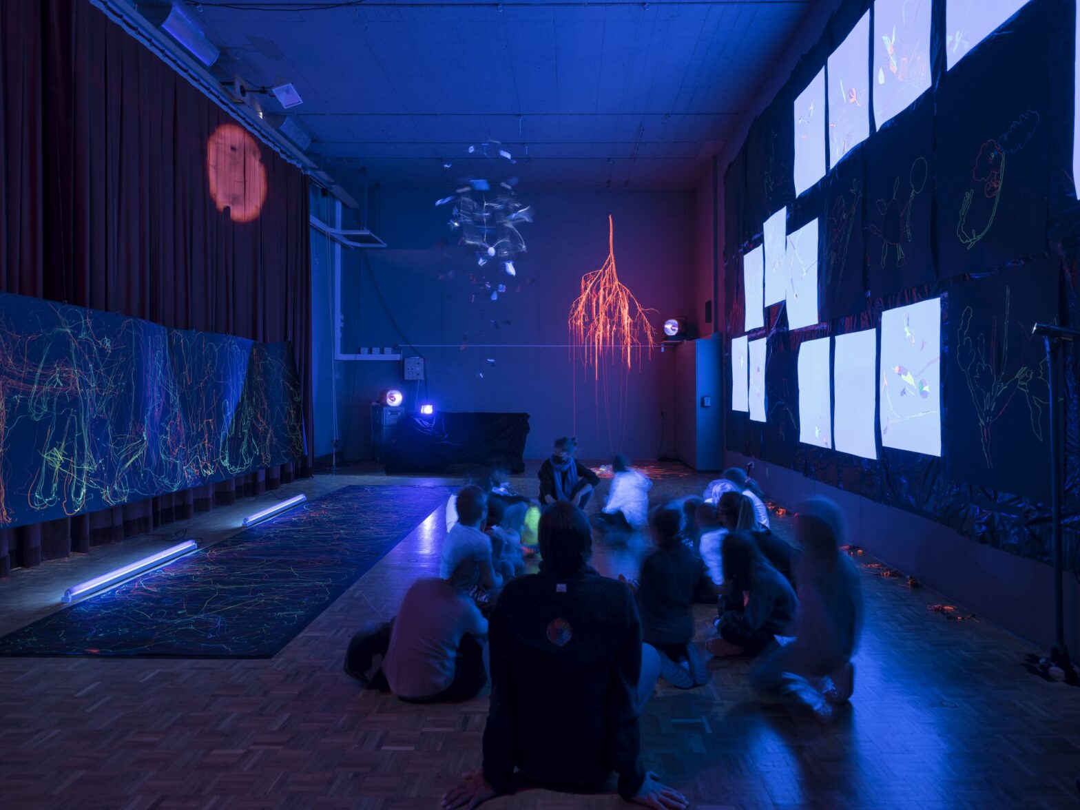 Kinder sitzen in einer mit Schwarzlicht beleuchteten Turnhalle