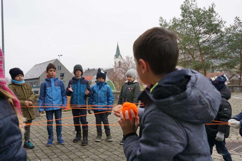 Schüler spannen mit orangener Wolle ein Netz.