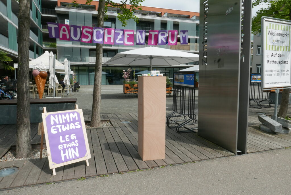 Zwischen zwei Bäumen im Stätischen Raum ist ein Banner aufgehängt mit der Aufschrift Tauschkiosk.
