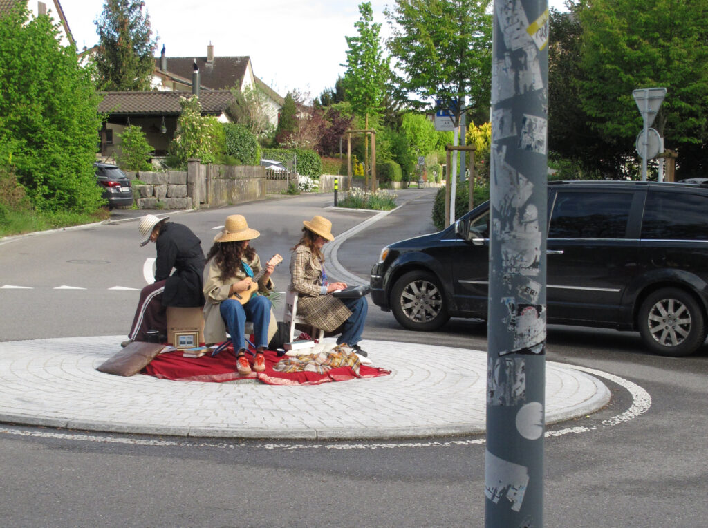 Drei Personen mit Hüten sitzen auf einem Kreisel und spielen Gitarre und Keyboard.