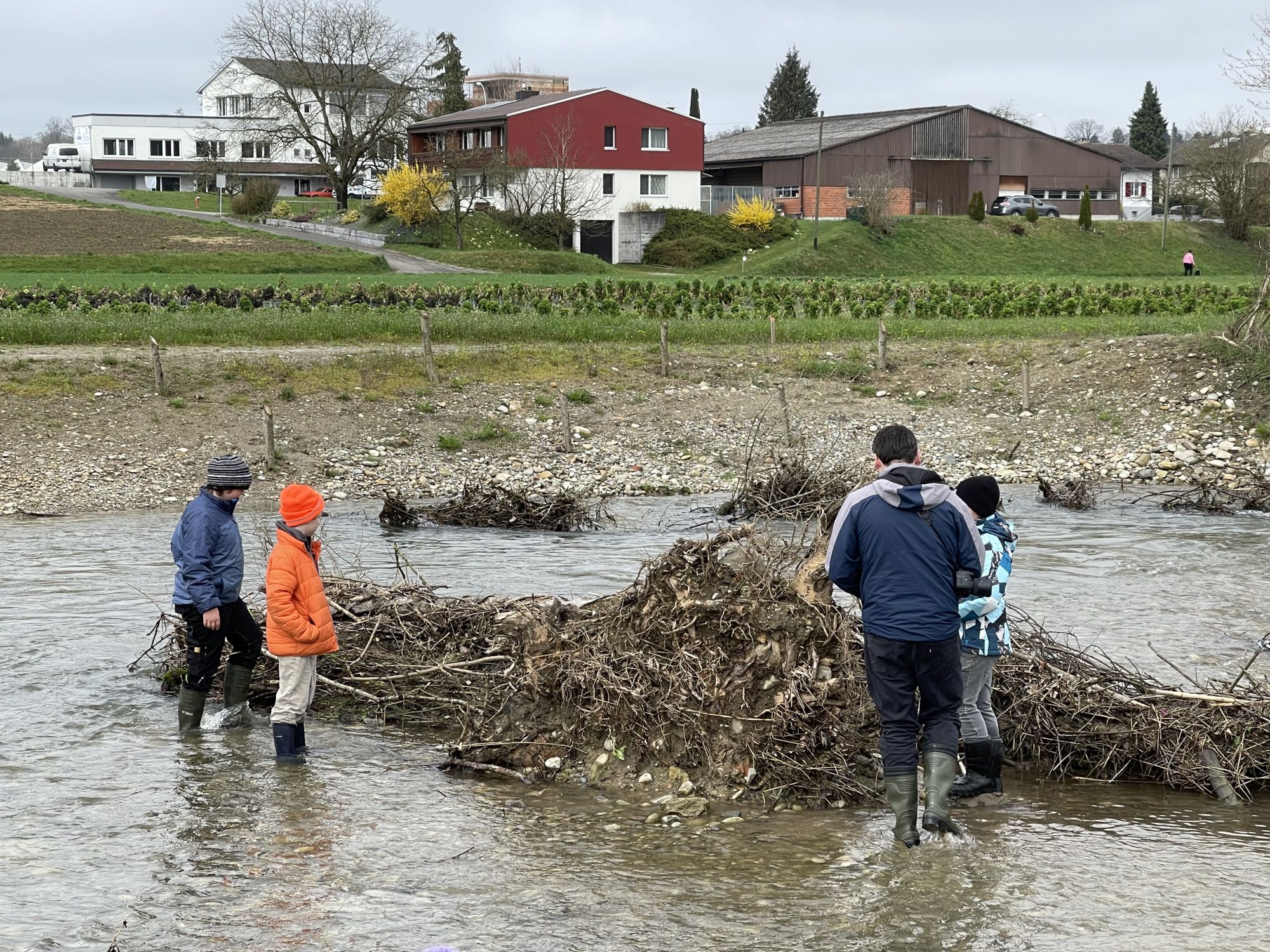 Schülerinnen und Schüler stehen mit Gummistiefeln in einem Fluss