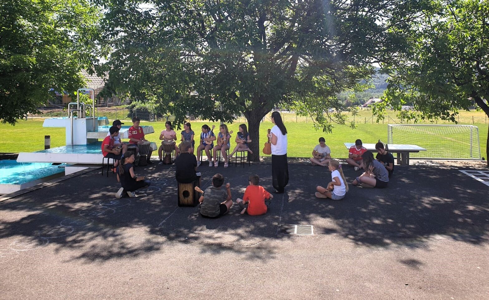 Schülerinnen und Schüler sitzen mit Instrumenten draussen in einem Kreis.