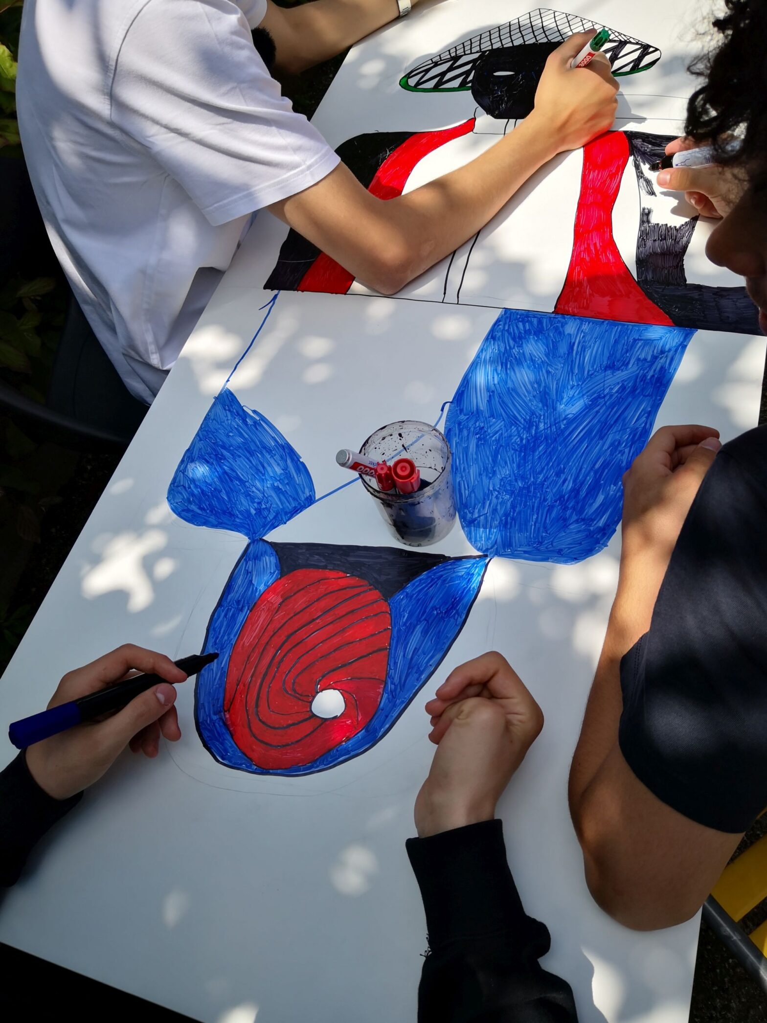 Jugendliche malen eine Figur mit Rot, Blau und Schwarz